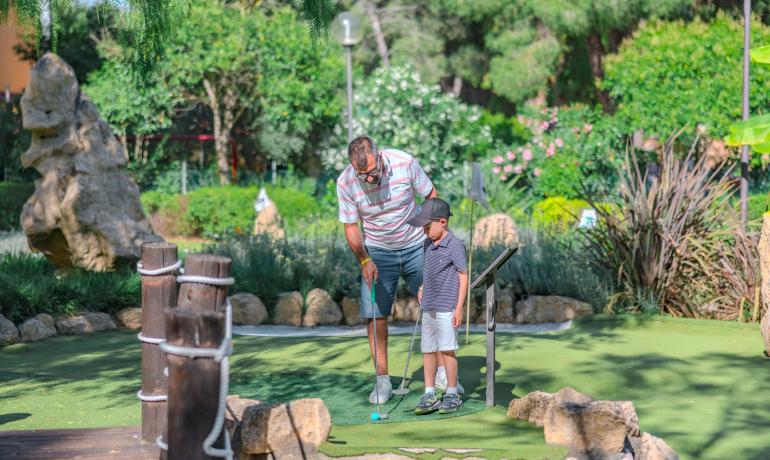 Uomo e bambino giocano a minigolf in un giardino verde.