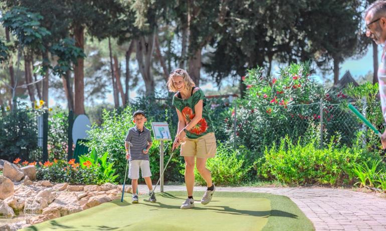 Famiglia gioca a minigolf in un giardino soleggiato.